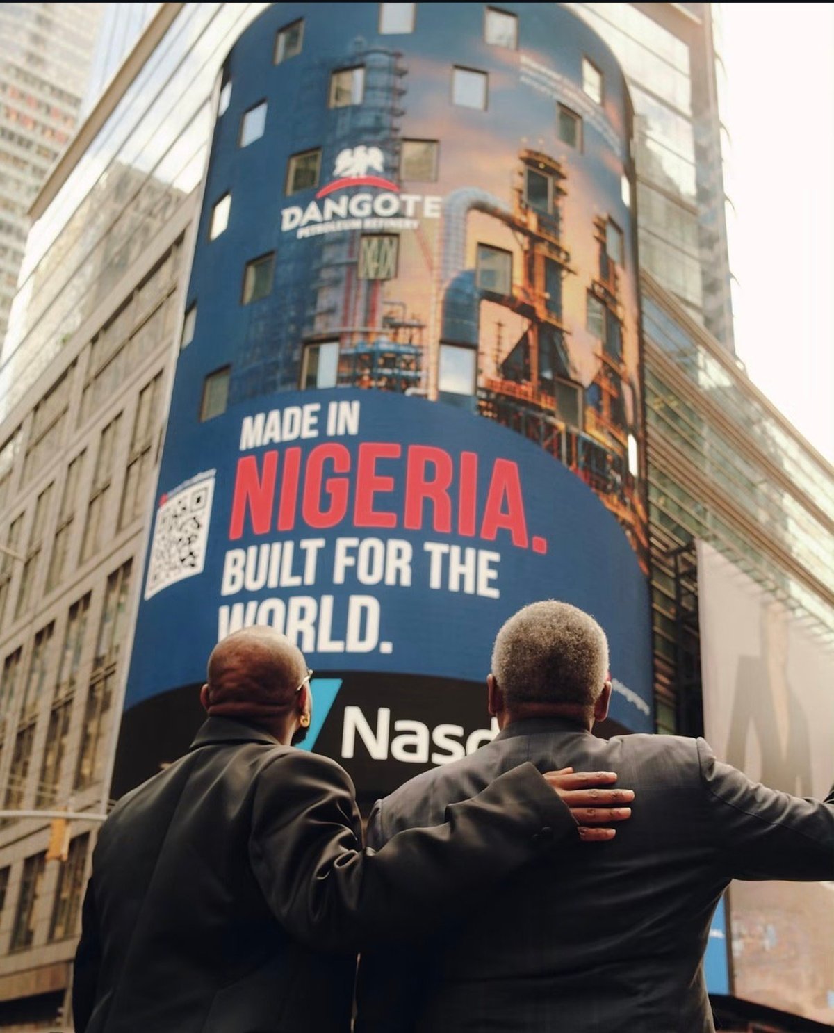 Two men viewing a large blue billboard advertising Made in Nigeria, Built for the World with Dangote and Naspers branding in an urban setting