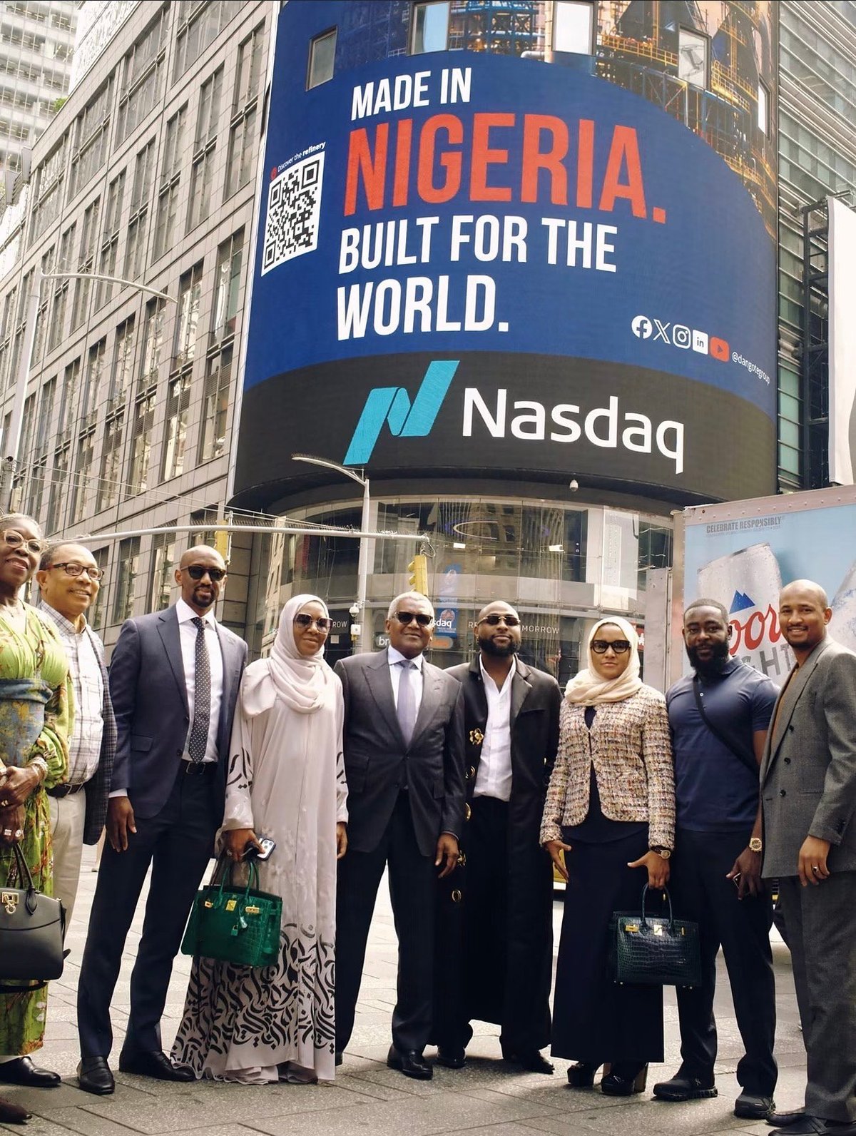 Group of well-dressed professionals posing beneath a large Nasdaq billboard reading Made in Nigeria. Built for the World. in Times Square.